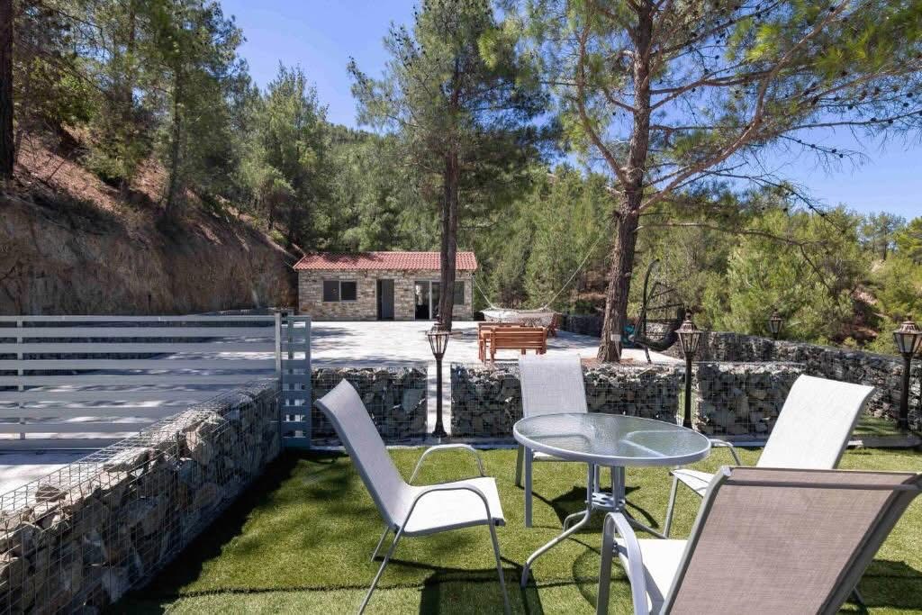 Lounge chairs and a glass table on the lawn terrace, looking back at the stone house